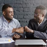 Business, teamwork and collaborataion concept. Two dark-skinned businesspeople in formal wear giving each other fist bump after successful agreement at meeting, happy with signing profitable contract